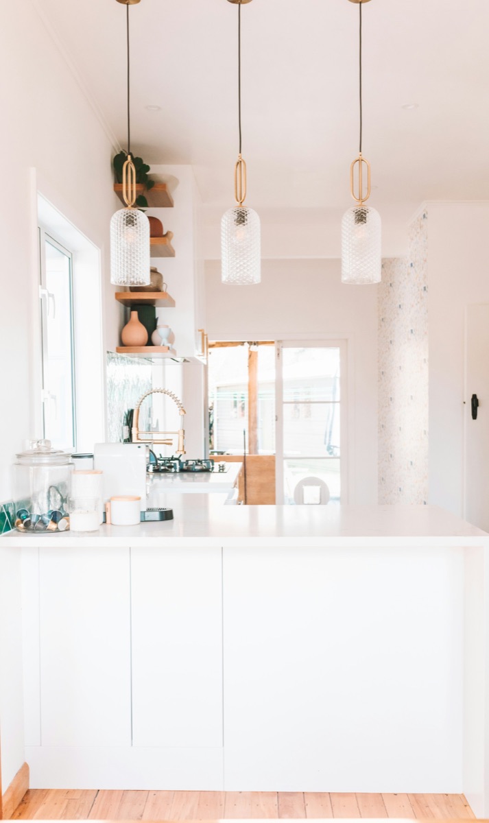 A bright white kitchen with glass pendant lights and pale wood shelves